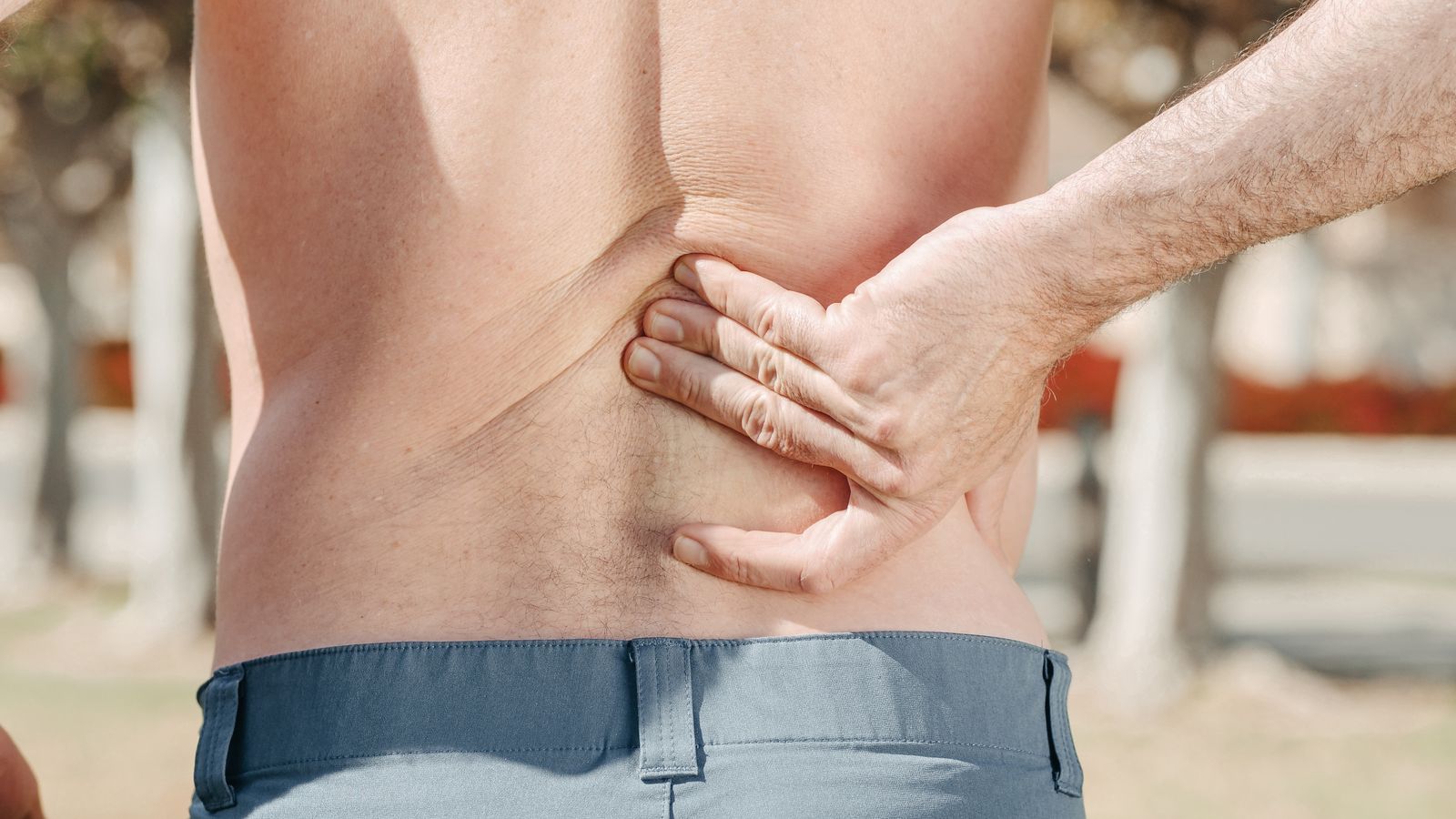 Man holding his lower back in discomfort, the common presentation of mechanical low back pain