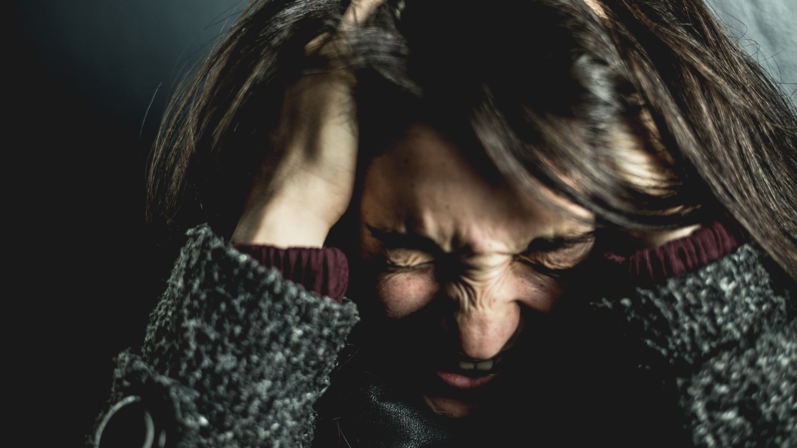 Stressed woman holding her head with both hands, illustrating stress-related hair loss