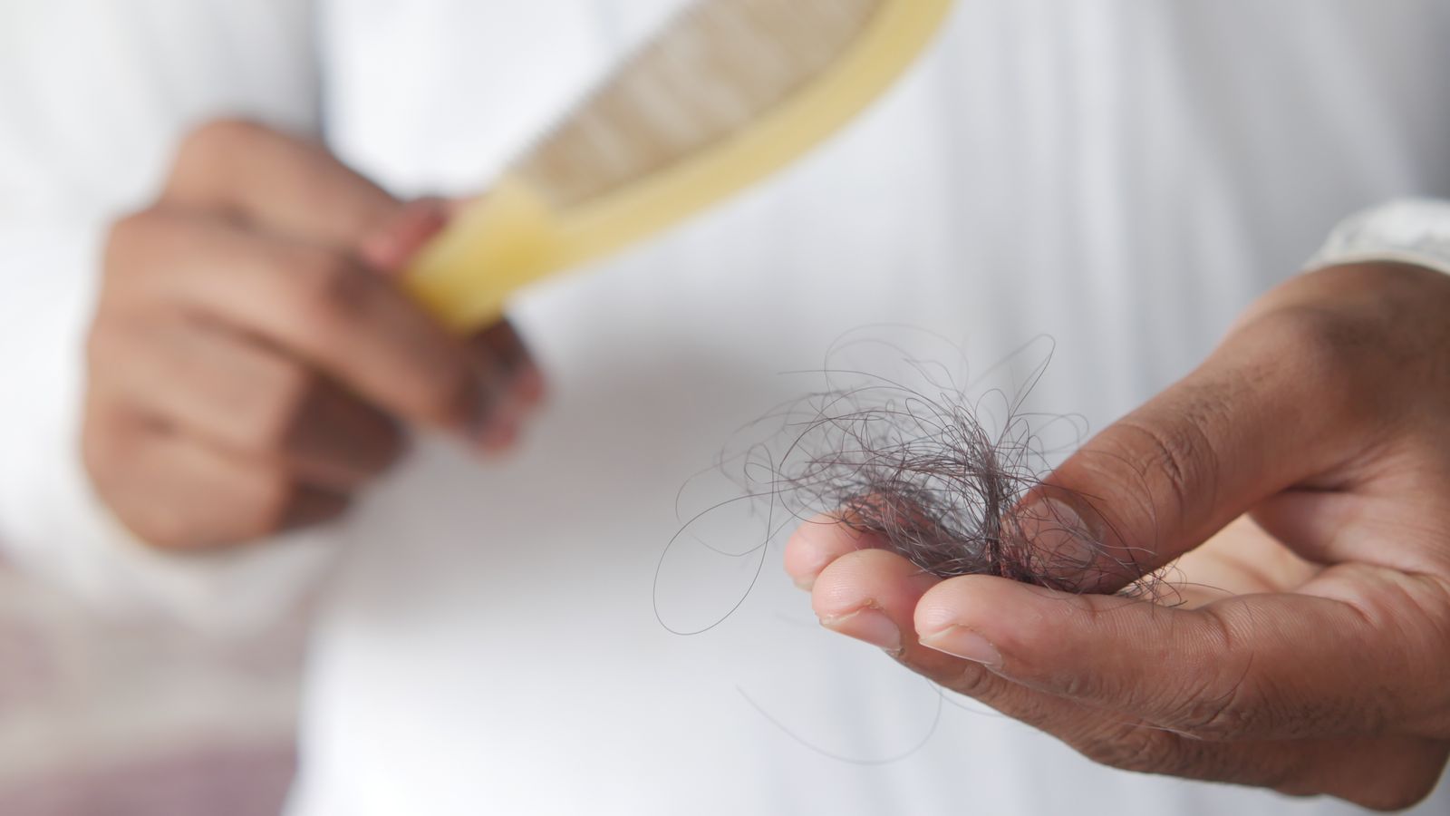 Hand holding a clump of fallen hair next to a comb, showing excessive hair fall