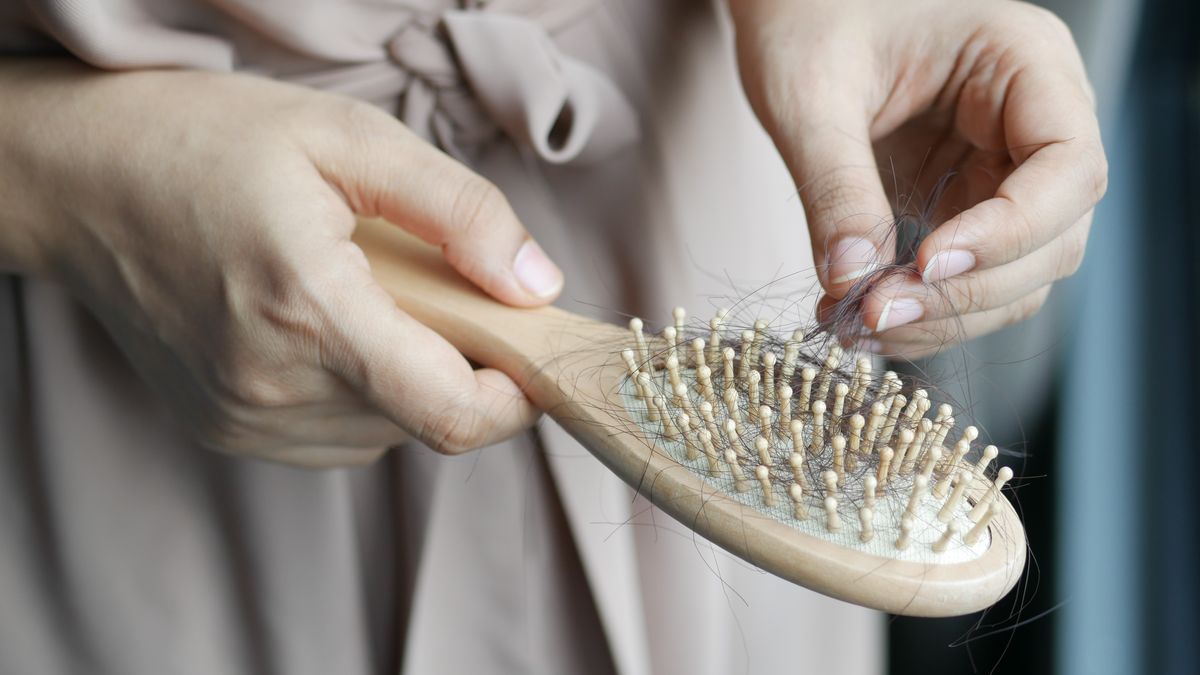 Woman removing shed hair from a wooden hairbrush