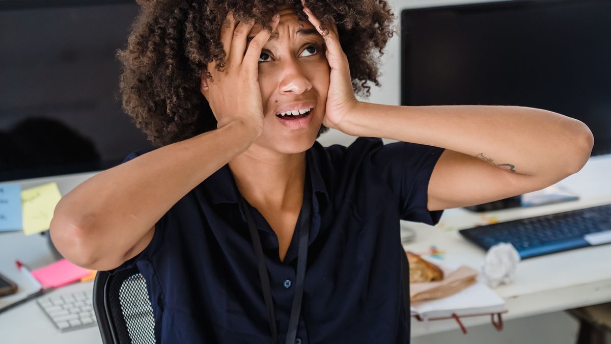 Woman at a work desk with her hands on her head, overwhelmed by work stress